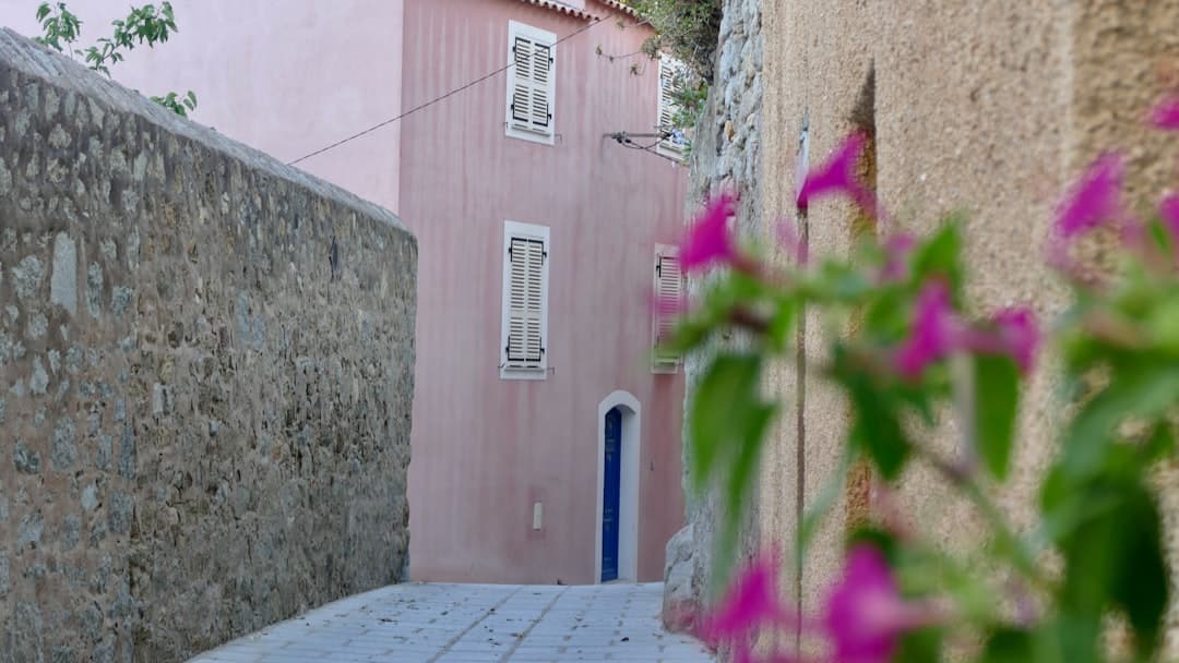A pink building sits on a narrow cobblestone street.